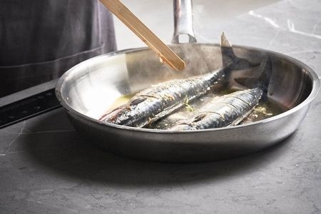 Ein Mann kocht mit der Invisacook Herfläche einen Fisch in einer Pfanne