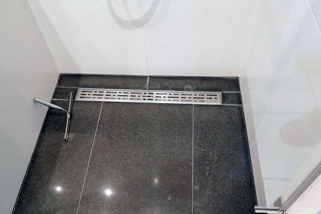 Dusche mit schwarzem Fliesenboden und Duschkopf, modern und elegant gestaltet.