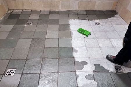 Eine Person reinigt einen Fliesenboden mit einem grünen Schwamm.